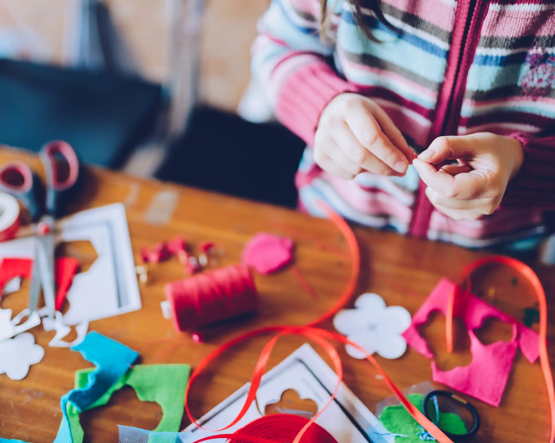 close up of persons hands with thread, scissors and ribbon on table. 